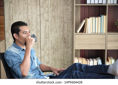 Handsome bearded guy is drinking coffee in a comfortable mood at his working place office.
