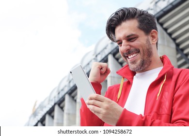 Handsome bearded hipster euphoric winner winning a betting and watching a smart phone with football stadium background. Man celebrate win a bet with a gambling mobile app. soccer bet, sports gambling. - Shutterstock ID 1094258672