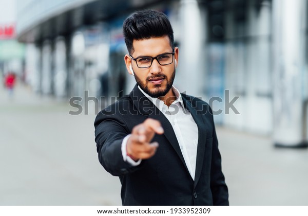 Handsome bearded\
Indian businessman directs his hand to the camera, looks to the\
camera, work, casual office,\
India.