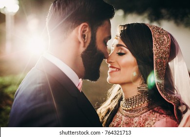 Handsome bearded Indian groom kisses bride in pink dress tender standing outisde