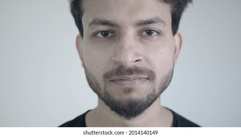 A Handsome Bearded Indian Guy Looking At The Camera With No Emotion On A White Wall Background
