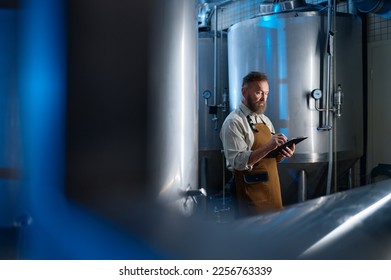 Handsome bearded man brewer inside modern beer factory around steel tanks
