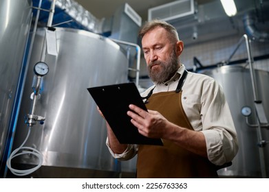 Handsome bearded man brewer inside modern beer factory around steel tanks - Powered by Shutterstock