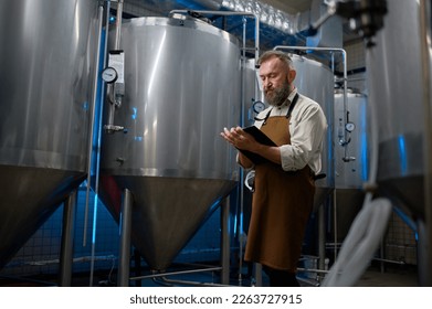 Handsome bearded man brewer inside modern beer factory around steel tanks - Powered by Shutterstock