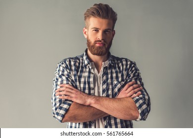 Handsome bearded man in casual clothes is looking at camera while standing with folded arms on gray background - Powered by Shutterstock