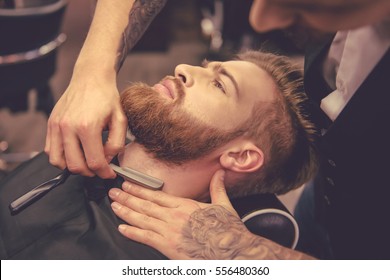 Handsome bearded man is getting shaved by hairdresser at the barbershop