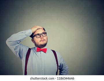 Handsome bearded man in glasses feeling stressed looking up in mindfulness on gray background