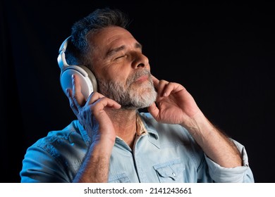 Handsome Bearded Man In Headphones Listening To Music. Close Up Portrait Of Cheerful Mature Man Enjoying Listening To Music Wearing Casual Jeans Outfit. Happy Man Smiling Listening To Music.