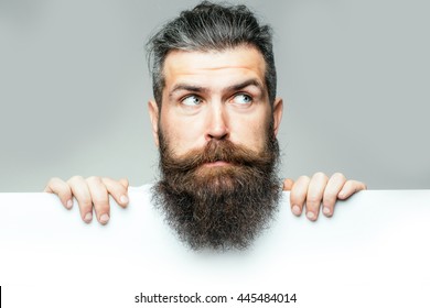 Handsome Bearded Man With Long Lush Beard And Moustache On Surprised Face With White Paper Sheet In Studio On Grey Background, Copy Space