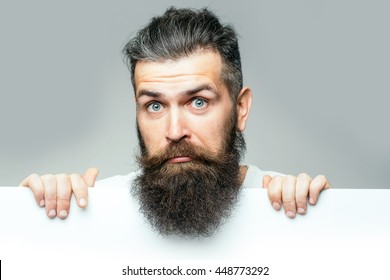 Handsome Bearded Man With Long Lush Beard And Moustache On Surprised Face With White Paper Sheet In Studio On Grey Background, Copy Space