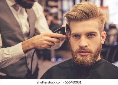 Handsome bearded man is looking forward while getting haircut by hairdresser at the barbershop - Powered by Shutterstock