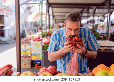 Handsome bearded man in plaid shirt choosing fruit at the market - Powered by Shutterstock