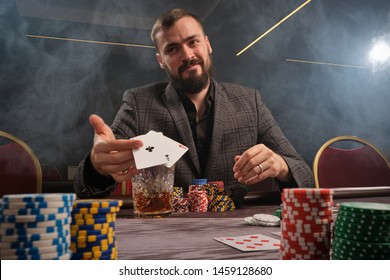 Handsome bearded man is playing poker sitting at the table in casino.