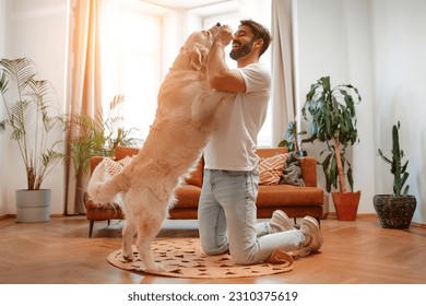 Handsome bearded man playing and training his labrador dog while sitting on the floor in the living room at home, having fun together.