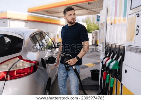 Handsome bearded man refueling car and looking on the scoreboard while standing on self service gas station