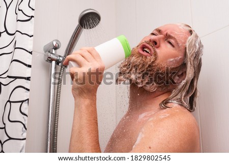 Handsome bearded man singing while taking shower at home using shampoo bottle instead of microphone. Happy caucasian guy sings with facial expression enjoying life