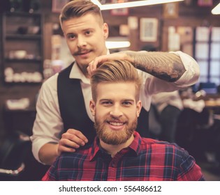 Handsome bearded man is smiling while having his hair cut by hairdresser at the barbershop - Powered by Shutterstock