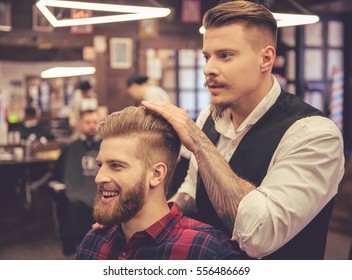 Handsome bearded man is smiling while having his hair cut by hairdresser at the barbershop - Powered by Shutterstock