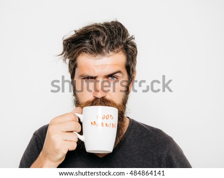 handsome bearded man with stylish hair beard and mustache on serious face in shirt holding white cup or mug with good morning text drinking tea or coffee in studio on grey background