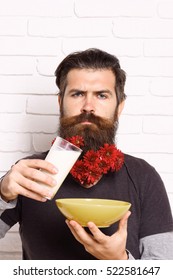 Handsome Bearded Man With Stylish Mustache And Long Beard With Red Autumn Flowers On Serious Face Holding Glass Of Milk With Yellow Bowl On White Brick Wall Background