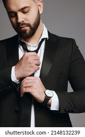 Handsome bearded man tightening tie on grey background