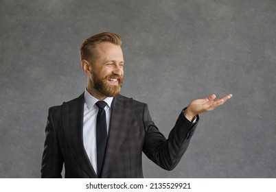 A handsome bearded man in a white shirt and black jacket with a smile demonstrates an imaginary product in the palm of his hand. The guy shows with his hand a possible product or text