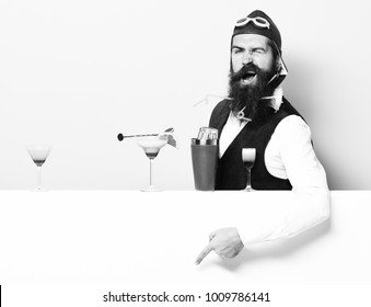 Handsome Bearded Pilot With Long Beard And Mustache On Funny Face With Shaker Alcoholic Cocktail In Vintage Suede Leather Waistcoat With Hand And Glasses On Purple Green Studio Background