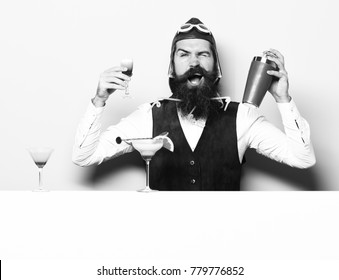 Handsome Bearded Pilot With Long Beard And Mustache On Funny Face With Shaker Alcoholic Cocktail In Vintage Suede Leather Waistcoat With Hand And Glasses On Purple Green Studio Background