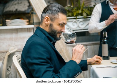 Handsome Bearded Rich Man With Stylish Mustache And Beard Holding Glass And Sniff Smell Of Red Wine At The Restautant.