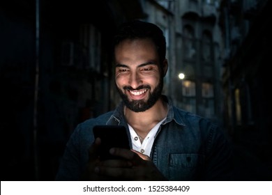 Handsome Bearded Smiling Man Holding Smartphone Outdoors Night Street, Light Reflection On The Face