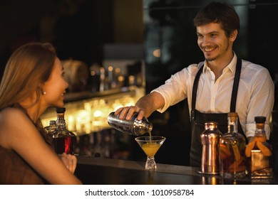 Handsome bearded young male bartender smiling joyfully talking to his beautiful female customer while pouring her a drink at the bar communication people lifestyle leisure service nightlife clubbing - Powered by Shutterstock