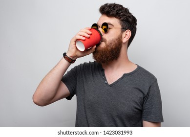 Handsome Bearded Young Man Drinking Coffee Or Tea To Go In A Paper Red Cup.