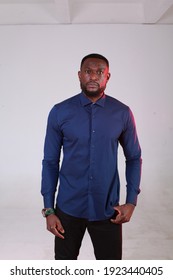 Handsome Black African Man In Casual Blue Shirt And Black Pants Posing Indoor On Grey White Background In Studio. Lifestyle