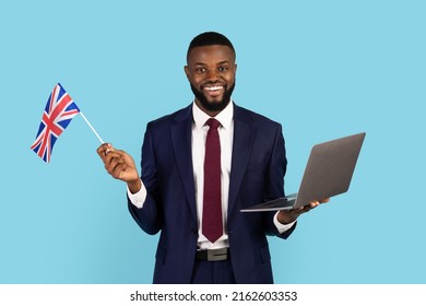 Handsome Black Businessman In Suit Holding Laptop And British Flag, Smiling African American Man Study Foreign Language Online, Enjoying Distance Learning, Posing Isolated Over Blue Background