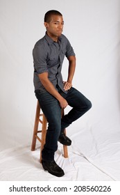 Handsome Black Man Sitting On A Wooden Stool And Looking Thoughtful