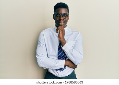 Handsome Black Man Wearing Glasses Business Shirt And Tie Looking Confident At The Camera With Smile With Crossed Arms And Hand Raised On Chin. Thinking Positive. 