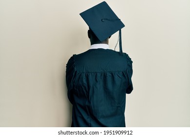 Handsome Black Man Wearing Graduation Cap And Ceremony Robe Standing Backwards Looking Away With Crossed Arms 