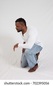 Handsome Black Man In White Shirt And Jeans, With A Thoughtful Expression Kneeling