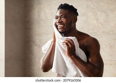 Handsome Black Man Wiping Face With Towel Looking Aside, Doing Facial Skincare Routine Standing In Modern Bathroom At Home In The Morning. Male Beauty Care Concept