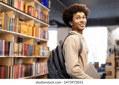 Handsome Black student guy in casual wear with backpack standing in library against background of bookshelves - Powered by Shutterstock