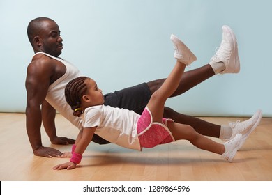 Handsome Black Young Father And His Cute Little Daughter Are Doing Reverce Plank With Leg Raise On The Floor At Home. Family Fitness Workout.