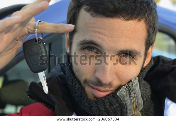 A handsome black-haired man  dressed in\
winter clothes holding a car key on his\
finger