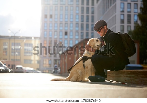 handsome blind guy have rest with golden\
retriever in the city, young male sit with guide dog, love him, dog\
assist him while\
walking