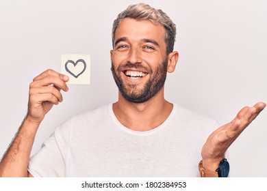 Handsome Blond Man With Beard Holding Reminder With Heart Shape Over White Background Celebrating Achievement With Happy Smile And Winner Expression With Raised Hand