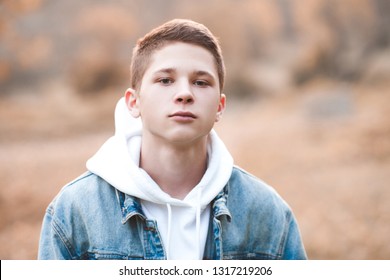 Handsome blond teen boy 16-17 year old wearing hoodie and denim jacket outdoors. Looking at camera. Spring season. 