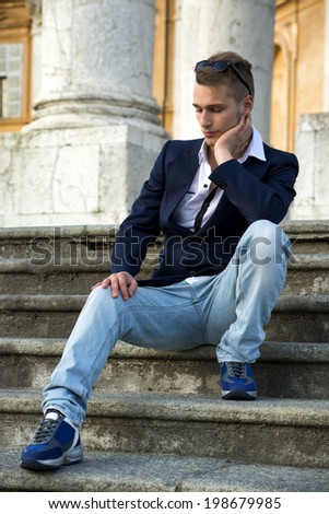Handsome blond young man with marble columns behind him, sitting on stair steps