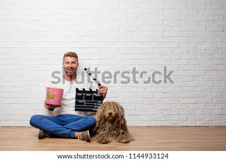 handsome blonde man with a dog and a pop corns bucket and a clapper. cimena concept
