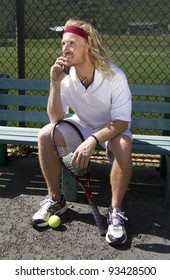 A Handsome Blonde Tennis Player Sits On The Sideline Bench And Chats On His Cell Phone