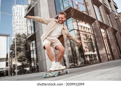 Handsome blonde young man doing tricks on skateboard trains on longboard outdoors at street with urban background. Excited laughing sporty skater practices outside. Extreme sport lifestyle concept. - Powered by Shutterstock