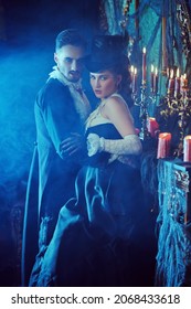 Handsome bloodthirsty male vampire going to bite an innocent beautiful waman in his arms. Dark vintage castle background. Halloween. Vampires of the 19th century. 